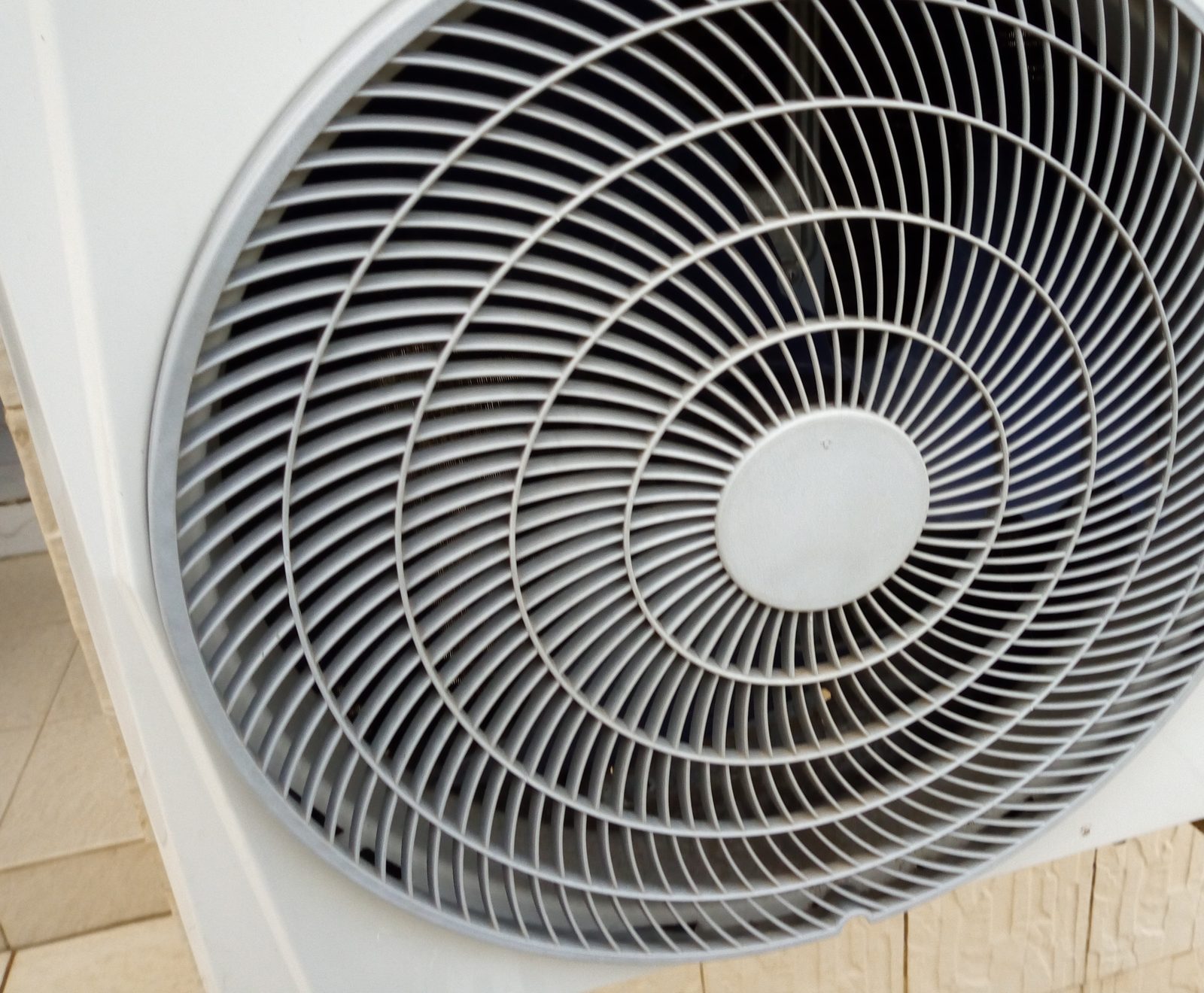 Unidade condensadora de ar-condicionado vista de perto, com a grade do ventilador